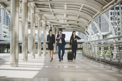 Full length of coworkers walking in office corridor