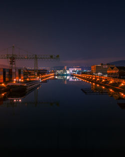 Illuminated city by sea against sky at night