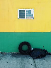 Garbage with tire on sidewalk against yellow wall