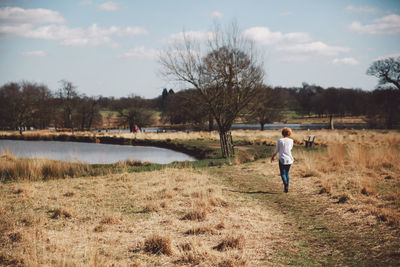 Rear view of young woman walking on field towards lake