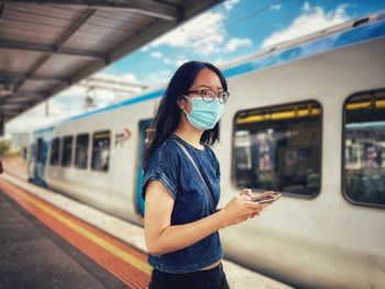 Portrait of asian woman in surgical mask using smartphone at train station platform 