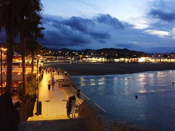 High angle view of illuminated town by sea against sky