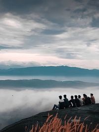 People standing on mountain by lake against sky