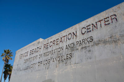 Low angle view of text on wall against clear blue sky