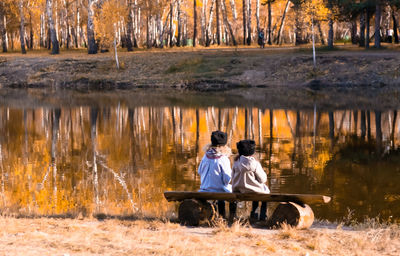 Friends sitting by lake during autumn