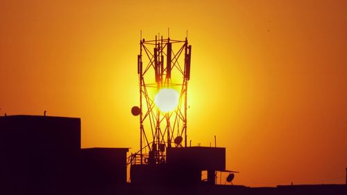 Low angle view of silhouette communications tower against orange sky