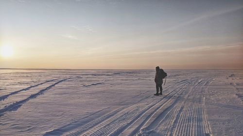 Rear view of man on snow covered land against sky during sunset