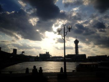 Silhouette of bridge over river against cloudy sky