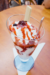 Ice cream with whipped cream and berry sauce in glass on table