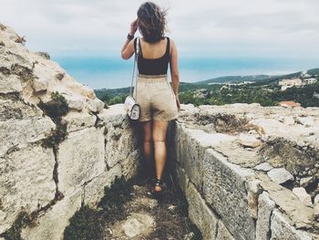 Rear view of young woman standing on rock against sky