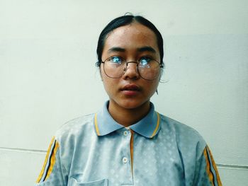 Portrait of young woman standing against wall