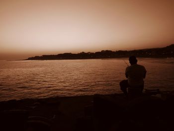 Rear view of silhouette man looking at sea against sky