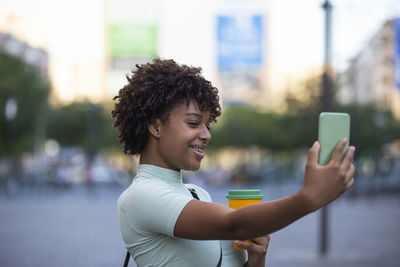 Making selfie. young woman with curly hair wearing fashionable clothes outdoors in the city.