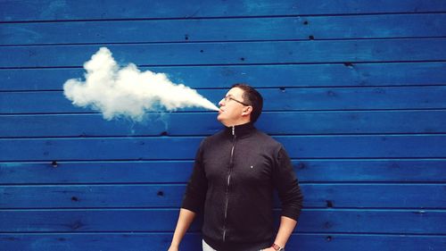 Full length of man smoking while standing against blue wall