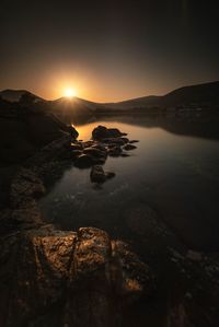 Scenic view of rocks on shore against sky during sunset