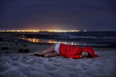 Woman sleeping at beach against sky during night