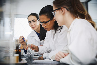 Female chemistry teacher explaining to young multi-ethnic students in laboratory