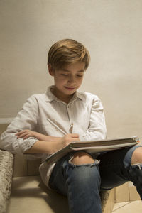 Boy sitting on book against wall