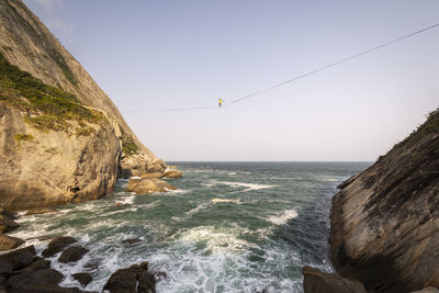 Beautiful view to highliner walking the line on rocky ocean shore