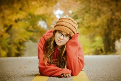 Portrait of girl wearing hat lying down on road 