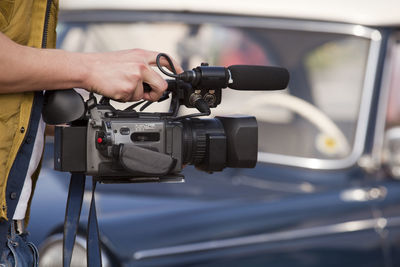 Midsection of journalist holding camera by car