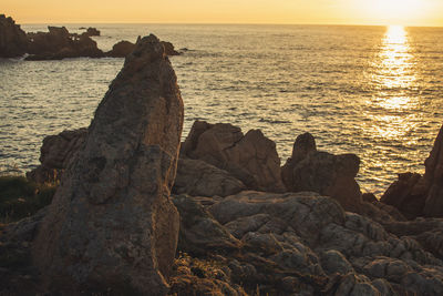 Rock formation on beach against sky during sunset