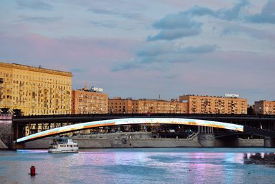 Bridge over river by buildings against sky during sunset