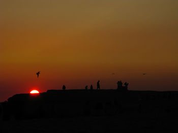Silhouette people on land against orange sky during sunset