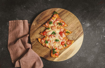 Pizza in the shape of a christmas tree on a cutting board with a kitchen napkin lies  on a dark