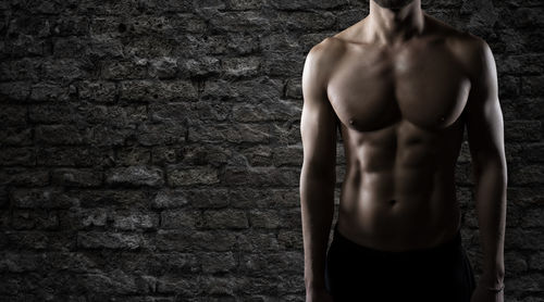 Full length of shirtless man standing against wall