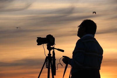 Rear view of man with camera against sky during sunset