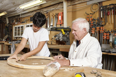 Carpenter teaching boy in workshop