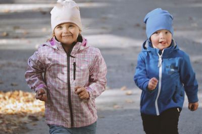 Cheerful siblings in warm clothes running outdoors