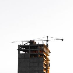 Low angle view of crane by incomplete building against clear sky