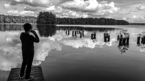 Rear view of people standing by lake against sky