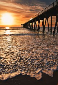 Silhouette bridge over sea against sky during sunset