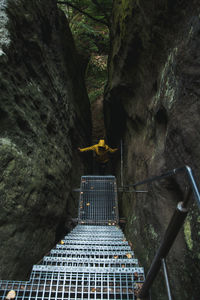 Hiker in yellow raincoat climbing up stairs amidst rocks