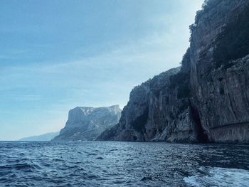 Scenic view of sea by mountain against sky