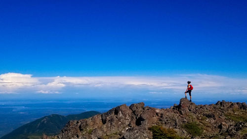 Woman standing on rock against blue sky