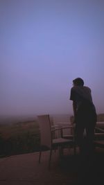 Rear view of man sitting on bench against sky