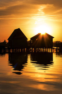 Silhouette houses in sea against orange sky