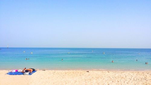 Rear view of people at beach against clear sky