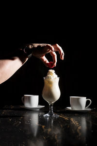 Close-up of hand holding coffee cup against black background