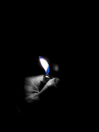 Close-up of hand holding lit candle in darkroom