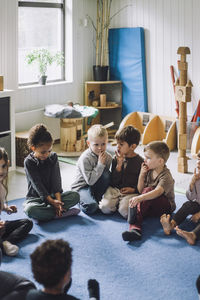 Multiracial boys and girls with fingers on lips sitting at kindergarten