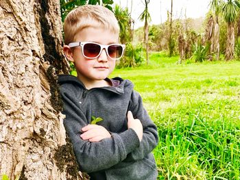 Portrait of boy wearing sunglasses standing against tree trunk