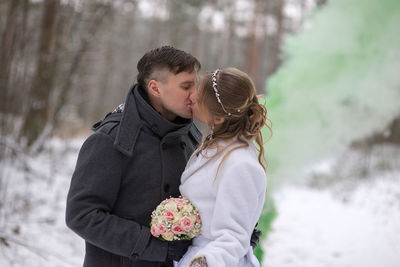 Man kissing woman while holding bouquet during winter