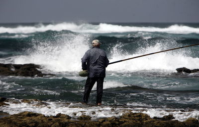 Man fishing while standing on sea shore