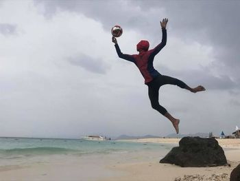 Man jumping at beach against sky