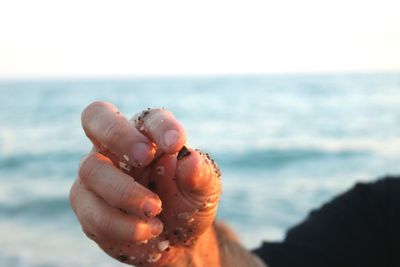 Cropped image of wet hand with sand against sea at beach